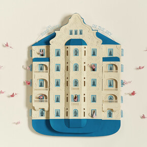 A handmade paper art piece of "The Bird Hotel In The Sky" with a multi-story building shape in cream and blue with open windows, balconies, and decorative cutouts, featuring pink paper birds flying around the building and peeking out of some windows.