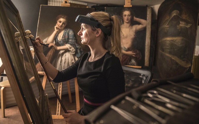 Sally holds a paintbrush in her hands and works on an oil painting