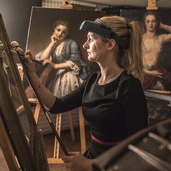 Sally holds a paintbrush in her hands and works on an oil painting