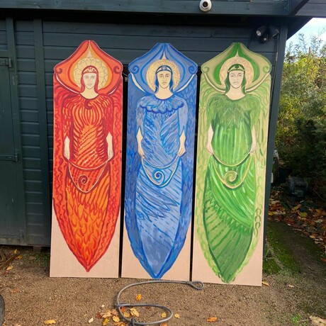 The three painted angels in shades of red, blue and green stood upright together