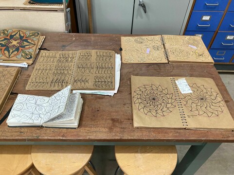 Four sketchbooks filled with geometric designs are laid out open on a table