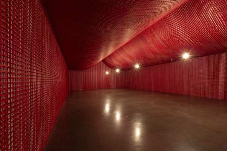 An empty red, bunker-like room lit by three bright bulbs. It is empty