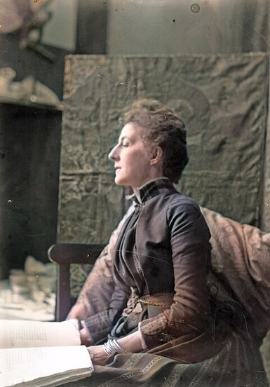 A colour photograph of Mary Watts sitting for her photo, you can see her left side profile and she is wearing her hair tied up and wearing a long dress