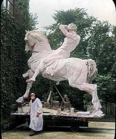 A colour photograph of George Watts stood in front of his sculpture 'Physical Energy'