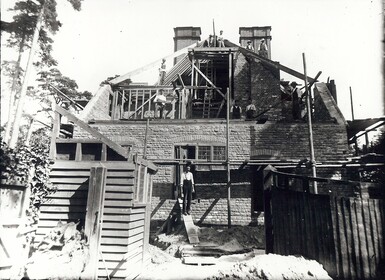 A black and white photograph of Limnerslease being constructed by hand, the photograph features men working hard on the roof of the building