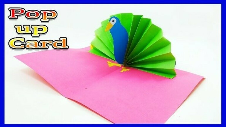 A colourful handmade pop-up card featuring a blue and green paper parrot with a fanned tail, sitting on a bright pink background. text at the top reads "pop up card.