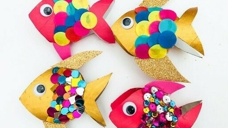Four colorful paper fish crafts decorated with sequins, googly eyes, and multicolored paper circles on a white background.