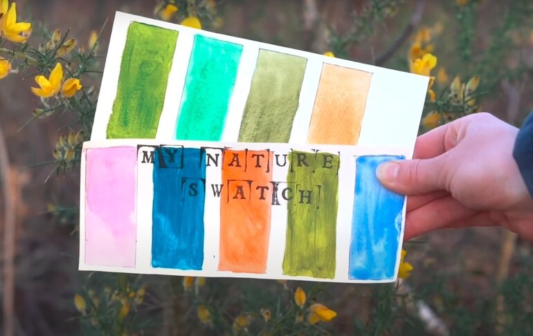 A hand holding a swatch book titled "my nature swatch" featuring various watercolour patches in shades of green, orange, pink, and blue, against a background of yellow flowers.