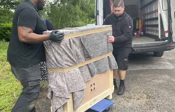 Two men pushing a wooden crate wrapped in a grey blanket towards a van