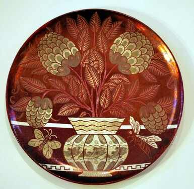 Red lustreware dish featuring a gold and cream coloured vase with dahlias in. There are two bees around the vase