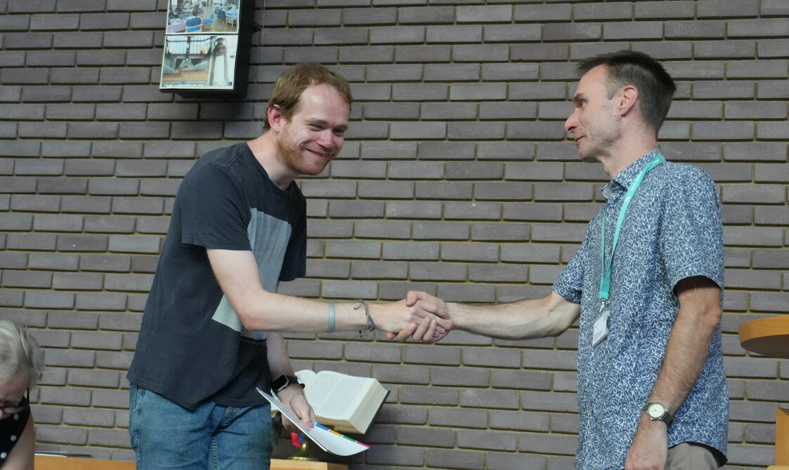 Two men are shaking hands and smiling, one man is holding a certificate