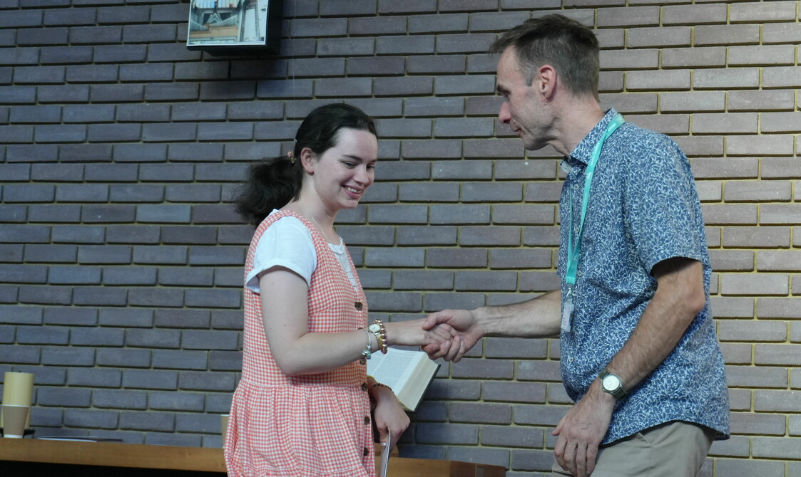 A woman in a pink dress is shaking hands with a man in a blue shirt