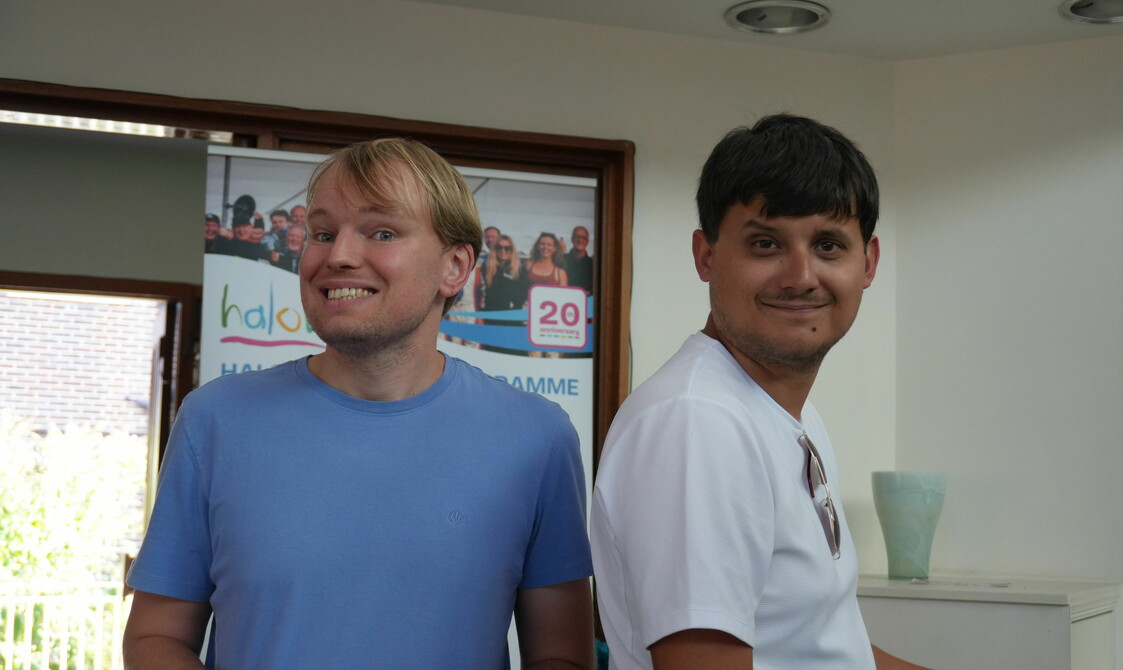 Two men are standing in front of a halow banner. Both are looking at the camera and smiling