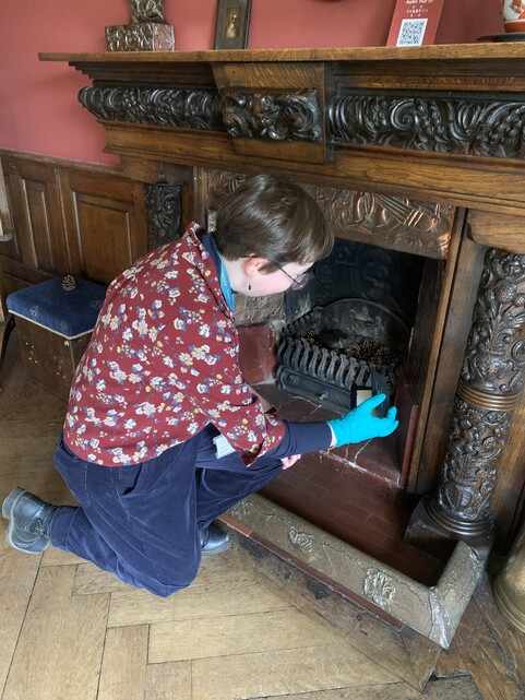 A woman in blue gloves kneeling by a fireplace