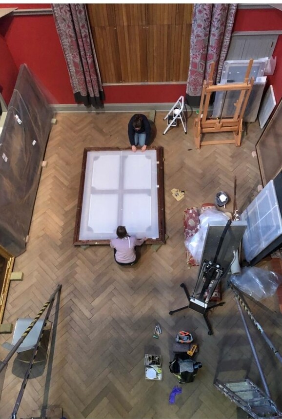 two figures frame a painting on the floor