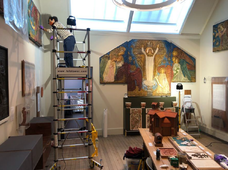 a figure on scaffolding adjusts a hanging picture