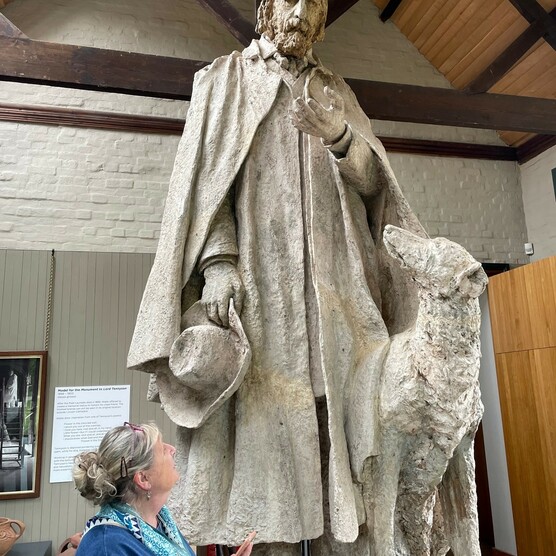 Jenny holds a phone and looks up at large sculpture of Tennyson