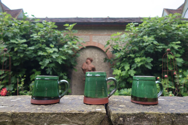 Three mugs with a green glaze lined up on the wall