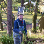 Chris holds a spade and is surrounded by plants