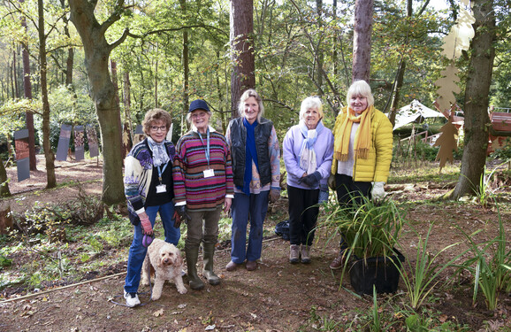 Five gardening volunteers and a dog pose for a photo in the woodlands