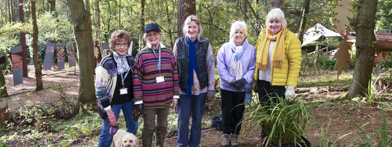 Five gardening volunteers and a dog pose for a photo in the woodlands