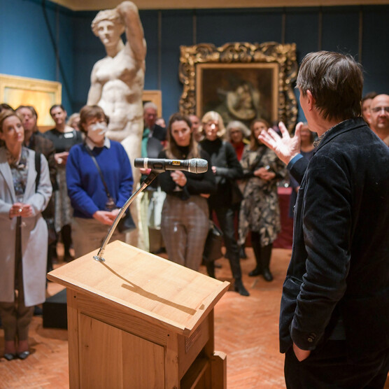 Xa, Director of the Ashmolean stands at the podium, he addresses a group of people in the gallery