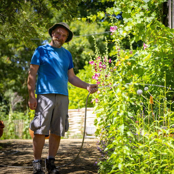 Chris smiles to the camera and waters flowers with hose