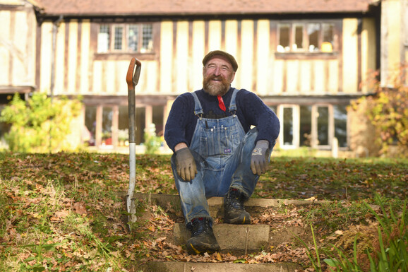 Chris smiles at the camera, sitting on a step with a spade next to him