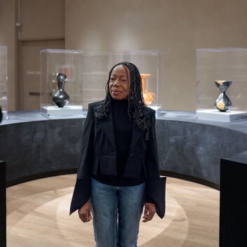A black woman, Dame Magdalene Odundo, stands in an art gallery