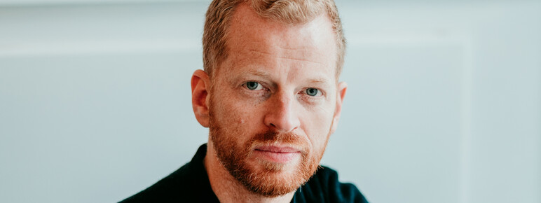 Matthew looks to camera with his arms folded