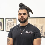 Artist Habib Hajallie in a black shirt wearing a gold necklace. He looks straight into the camera