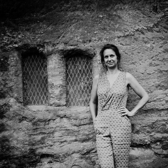 Black and white tintype portrait of a woman standing by an old stone wall