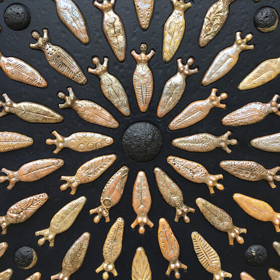 A bronze and black artwork featuring women shapes in a circular pattern