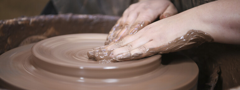A close up of Ashleigh shaping clay on a pottery wheel