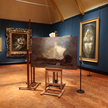 A collection of paintings on easels placed in the centre of the Watts Historic Gallery as part of an intervention
