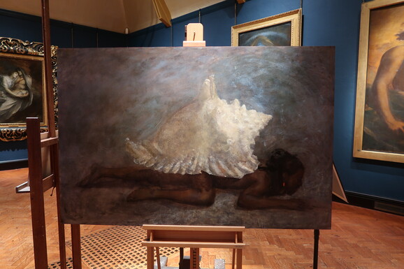 An oil painting on an easel of a large sea shell on the back of a sprawled, dark figure.