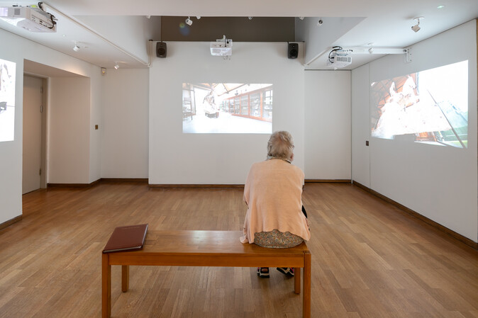 A visitor sits on a bench and watches the video installation