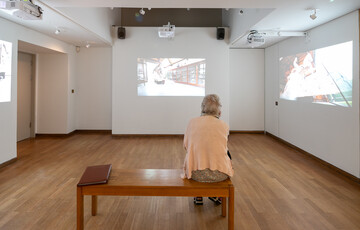 A visitor sits on a bench and watches the video installation