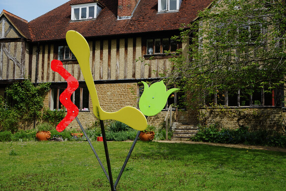 Photo of Limnerslease with an abstract sculpture on the lawn in front. The sculpture consists of red, yellow and green perspex in abstract shapes on metal poles