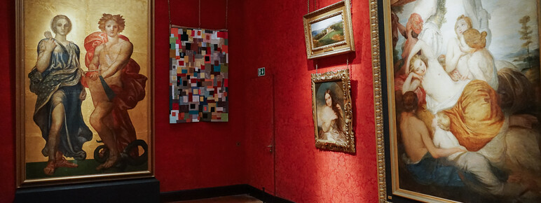 Photo inside the Historic Galleries at Watts Gallery. A multicoloured textiles artwork is hung beside a painting.