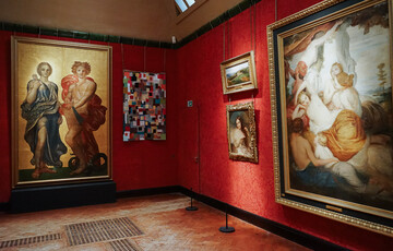 Photo inside the Historic Galleries at Watts Gallery. A multicoloured textiles artwork is hung beside a painting.