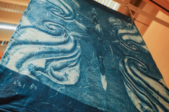 Cyanotype hanging from the ceiling of Watts Gallery with beading decorating the bottom of the fabric. There is an abstract design on the fabric