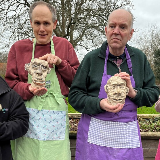 Four people holding their ceramic work and smiling at the camera