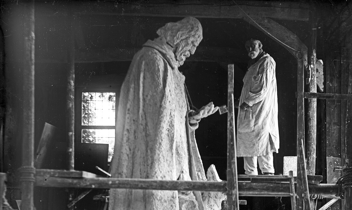 Black and white photo of artist G F Watts on scaffolding next to large statue of Lord Tennyson