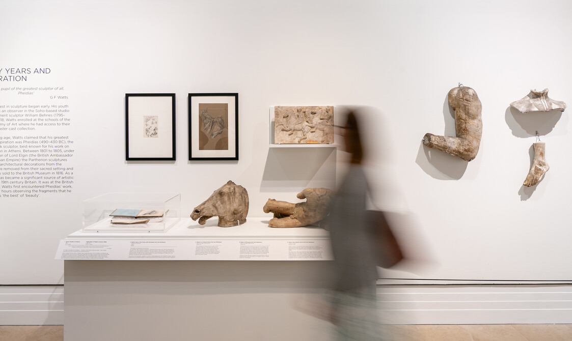 A blurred figure walks past a display in the Fragmented Legacy exhibition