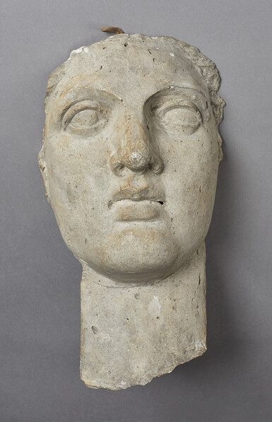 A carved face and neck of a young woman, the eyes are open but there is no detail