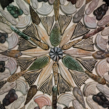 Photo of a ceramic tile installation by Kay Aplin. It features abstract shaped tiles in a mandala pattern