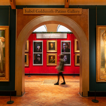 Portraits hung on a red wall with a visitor walking past