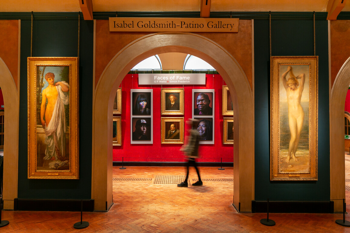 Portraits hung on a red wall with a visitor walking past