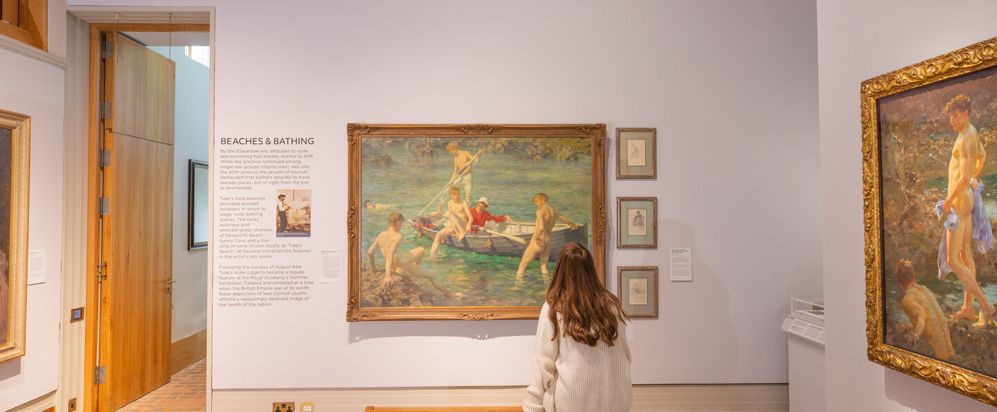 A visitor sits on a bench in front of a large beach scene painting